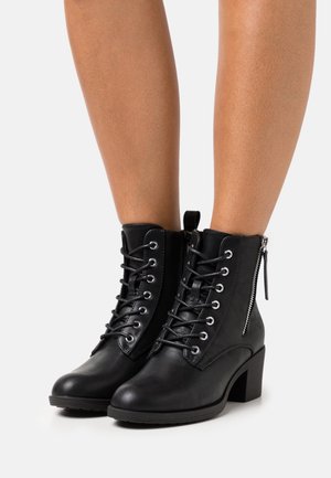 Bottines noires en simili cuir, avec un laçage à l'avant, une fermeture éclair sur le côté et un talon épais pour un soutien et une stabilité.