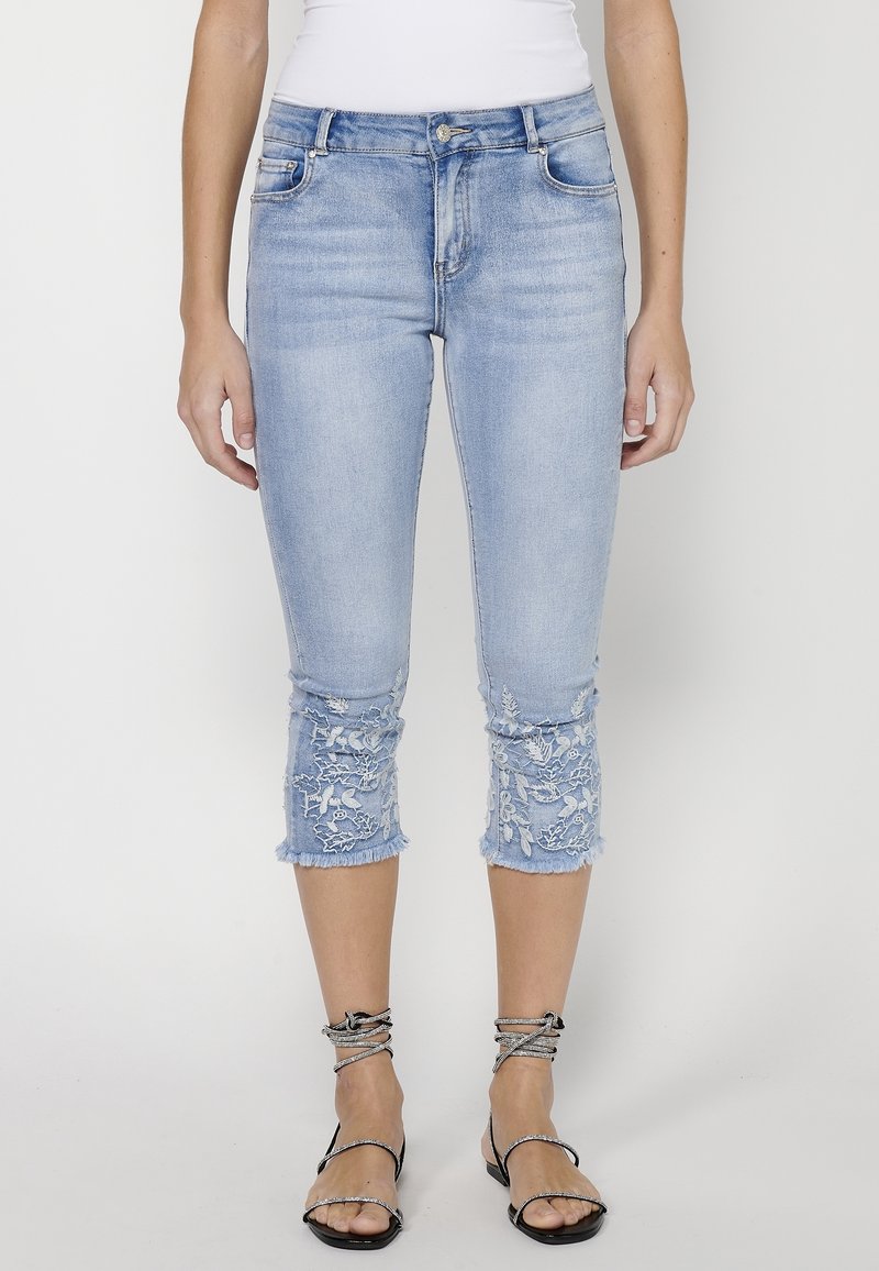 Light blue denim cropped jeans with embroidered floral designs at the cuffs and frayed hems; fitted silhouette with standard five-pocket styling.