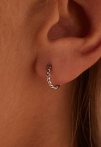 Boucle d'oreille en argent avec un design torsadé, s'adaptant parfaitement au lobe, mettant en valeur une finitionpolie et une texture lisse.
