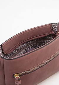 Bolso de imitación de cuero marrón con cierre de cremallera, con un forro de tela de patrón floral y un bolsillo exterior con cremallera. Textura suave.