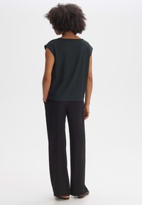 Top nero testurizzato con maniche a raglan, abbinato a pantaloni neri larghi. L'outfit presenta una silhouette rilassata e sottili dettagli di design.