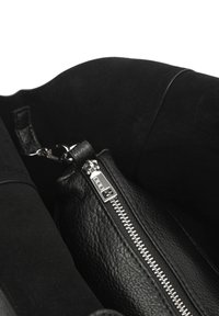 Interno di una borsa a tracolla nera in pelle, con materiali lisci e testurizzati, dotata di una zip argentata e di una borsa interna rimovibile.