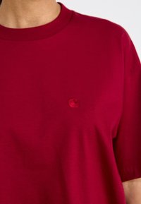Tricou din bumbac roșu, cu guler rotund, mâneci scurte și un logo brodat subtil pe partea stângă a pieptului. Textură fină, culoare uniformă.
