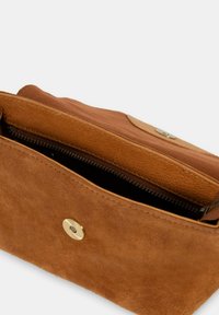 Tasche aus hellbraunem Wildleder mit einem Reißverschlussfach, einem magnetischen Druckverschluss und einem glatten Innenfutter. Minimalistisches Design und klare Kanten.