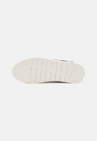 Shoe outsole featuring a textured rubber sole in white with structured grooves and a small logo imprint on the side.