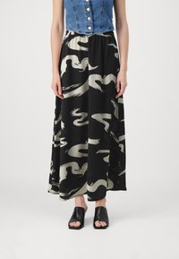 Jupe maxi en tissu noir avec un motif abstrait crème, taille élastique, associée à un crop top en denim et des chaussures ouvertes noires.
