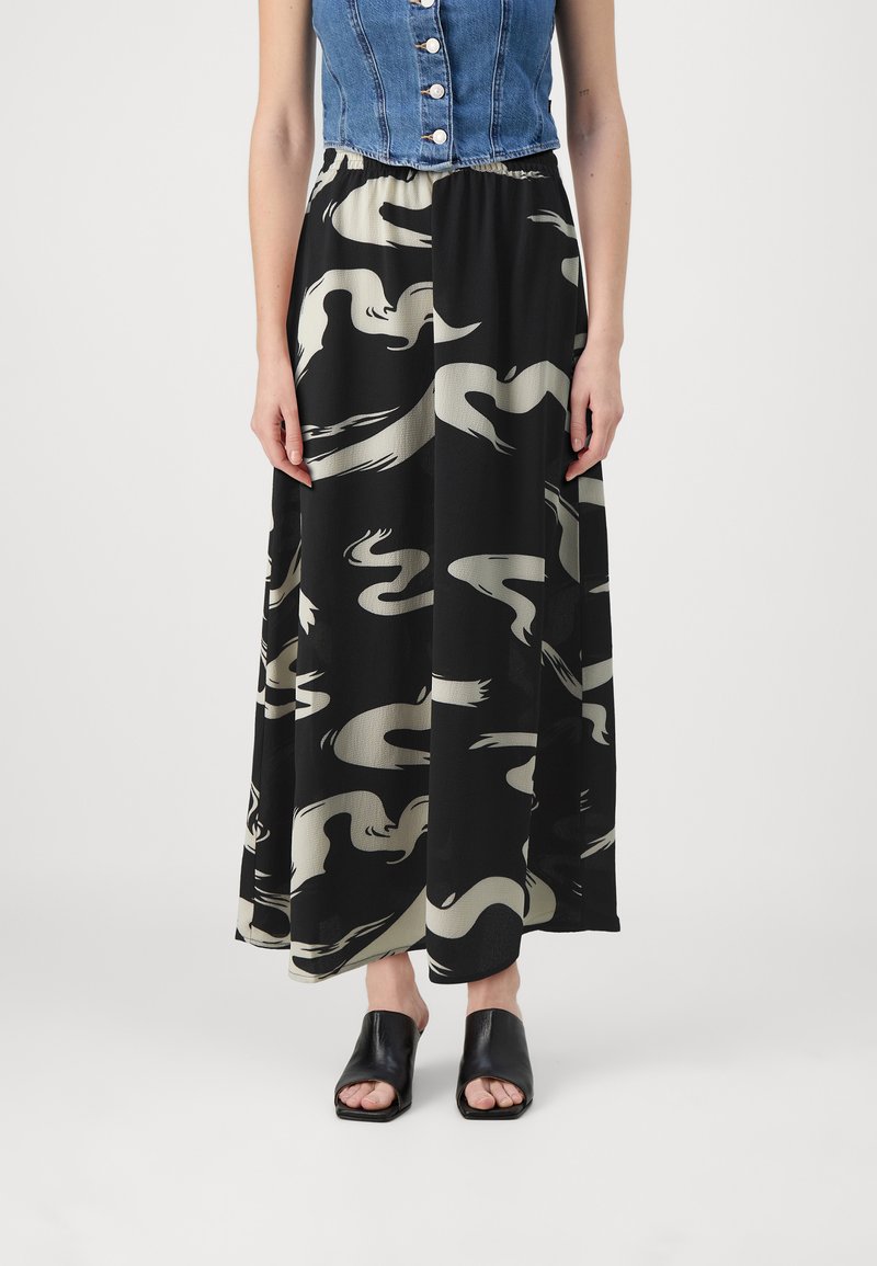 Jupe maxi en tissu noir avec un motif abstrait crème, taille élastique, associée à un crop top en denim et des chaussures ouvertes noires.