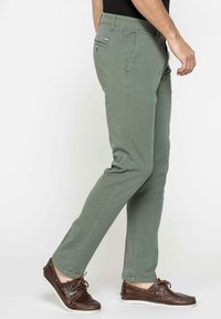 Pantaloni verdi in cotone da uomo con vestibilità slim, dotati di tasche laterali e tasca posteriore, abbinati a scarpe da barca in pelle marrone.
