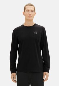Zwarte T-shirt met lange mouwen van zachte stof, voorzien van een ronde halslijn en een klein rond logo op de borst, met aansluitende mouwen en een gladde textuur.