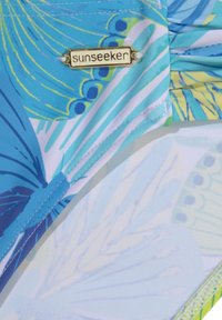 Badebekleidung aus einem blauen, grünen und gelben Butterfly- gemusterten Stoff mit einem metallischen "Sunseeker"-Label und kontrastierenden Nähdetails.
