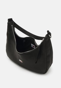 Bolso de hombro negro de cuero con una textura suave, forma curva, cierre de cremallera y una correa de tela. El interior cuenta con un pequeño bolsillo con cremallera.