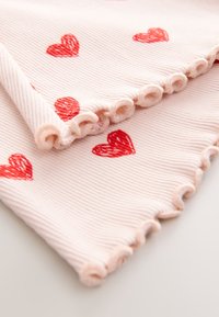 Ružová rebrovaná tkanina s volánovým okrajom, zdobená červenými srdiečkami. Hladká textúra so subtílnymi pruhmi, zložená na sklad.