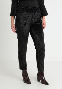 Svarta sammetsbyxor med en blank yta, med dragsko i midjan och slim fit. Tillsammans med glänsande klackade ankelstövlar.