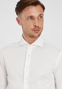 Witte blouse met lange mouwen, gemaakt van gladde stof, met een standaard kraag, knoopsluiting aan de voorkant en subtiele stikdetails.