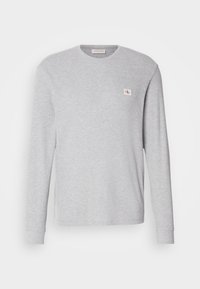 Pull à col rond à manches longues gris clair avec une texture subtile en maille gaufrée et un petit patch logo Calvin Klein rouge et blanc sur le côté gauche de la poitrine.