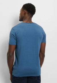 T-shirt in cotone blu con maniche corte, scollo rotondo e una texture liscia. Presenta un piccolo dettaglio con etichetta sul lato inferiore della cucitura.