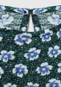 Pritisnjen posnetek modrega in belega cvetličnega vzorca tkanine z zelenimi pikami, ki ima majhen ključni odprtini pri izrezu.