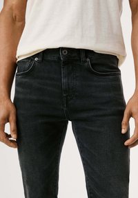 Tummat farkut slim fit -mallilla, joissa on klassinen viisi-tasku design ja hienovaraiset haalistumat. Yhdistelmässä on vaaleansävyinen t-paita.