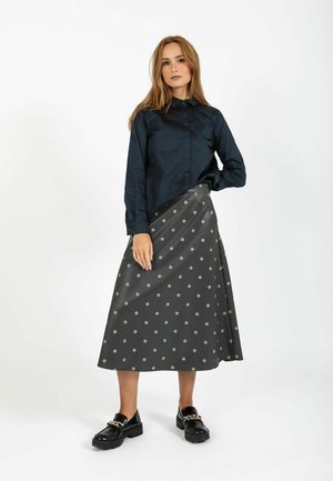 Marineblå langærmet skjorte kombineret med en sort maxinederdel med grønne polkaprikker. Sorte sko med kædedetalje. Enkel og moderne design.