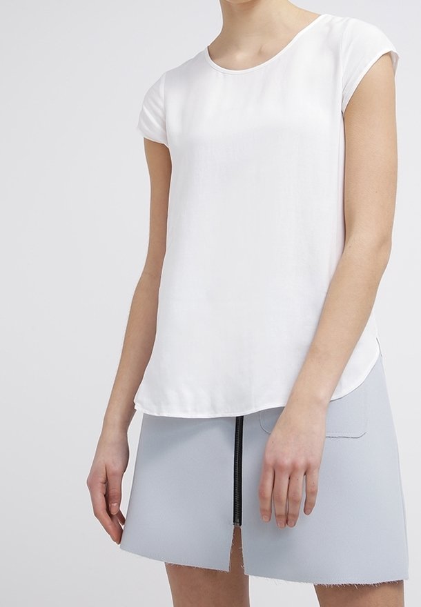 Witte top met korte mouwen en een ronde hals, gemaakt van een gladde stof. Gecombineerd met een lichtgrijze minirok met een ritsdetail.