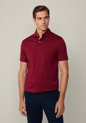 Bordo polo majica s kragnom, s tri gumba i kratkim rukavima, napravljena od mekog materijala. Nosite je uz tamnoplave hlače.