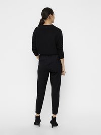 Suéter negro de punto con mangas largas, combinado con pantalones oscuros de textura y botas negras hasta el tobillo. El conjunto presenta un corte relajado y líneas limpias.