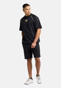 Black cotton t-shirt with short sleeves and logo on the chest, paired with matching black shorts and white sneakers.