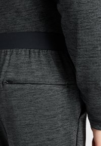 Grijze sportkleding heeft een textuurstof met een subtiel patroon, een elastische tailleband en een zak met rits aan de achterkant.