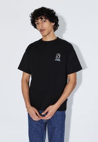 Black cotton t-shirt with a round neckline, short sleeves, featuring a white embroidered graphic on the chest. Loose fit.