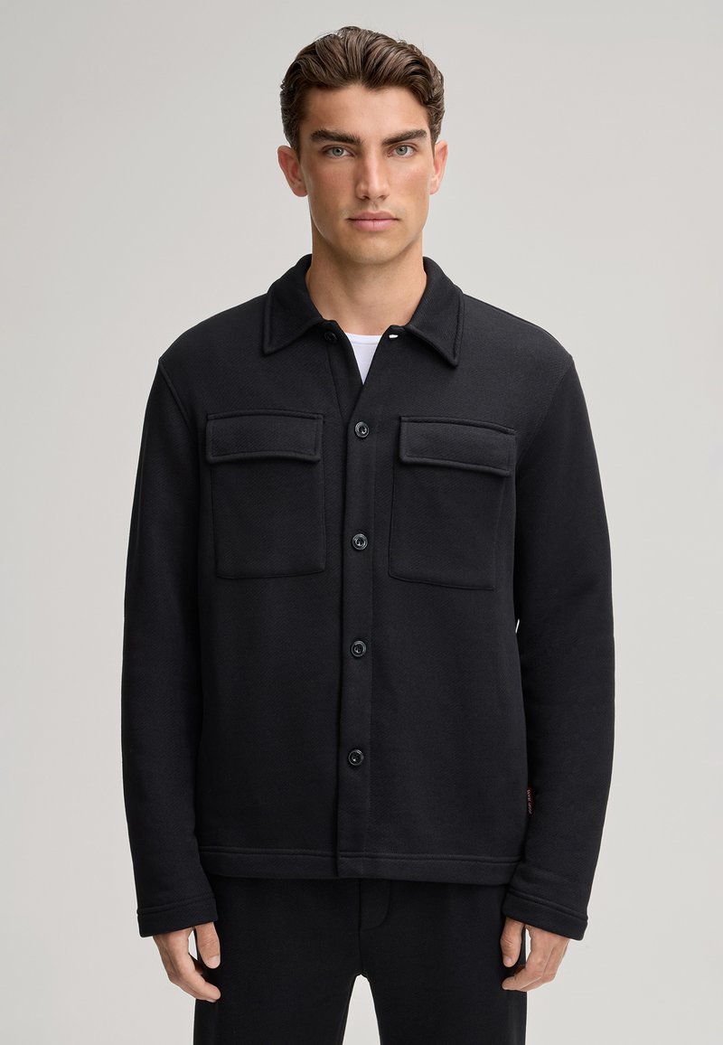 Giacca in pile nera con chiusura a bottoni, due tasche sul petto e un collo elegante. Tessuto morbido e design casual adatto per essere indossata a strati.