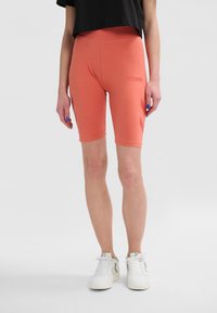 Pfirsichfarbene Radfahrshorts aus dehnbarem Material, mit einem hohen Bund und einem dezenten Logoaufdruck an der Seite.