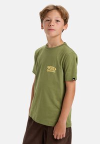 Green cotton T-shirt with a round neckline, short sleeves, and a yellow logo print on the chest. Textured fabric with a relaxed fit.