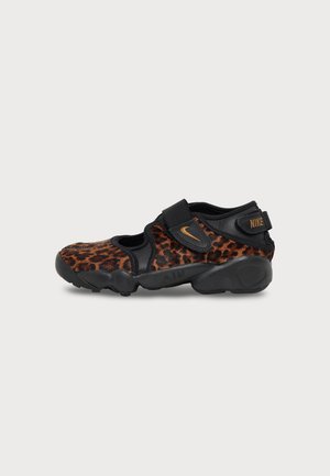 Vue de profil d’une chaussure Nike noire avec des empiècements à imprimé léopard, des détails dorés, des brides réglables à fermeture autoagrippante et une semelle épaisse sculptée.