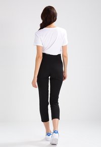 Svarta skräddarsydda byxor med hög midja, kombinerade med en vit t-shirt och vita sneakers med blå accenter. Slät, åtsittande design.