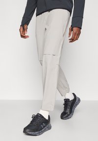 Világos bézs színű cargo nadrág, amely tapered (keskenyített) szárakkal rendelkezik, oldalsó zsebekkel. Fekete sportcipővel és fehér bokazoknival viselve. Texturált sötét felső.