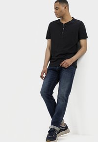 T-shirt henley noir à manches courtes avec trois boutons associé à un jean en denim bleu et des baskets sombres, créant une tenue décontractée.