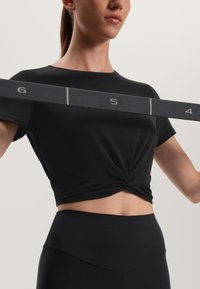 Fekete cropped póló, csavart első részével, magasderekú fekete leggingsszel párosítva, amelyek sima textúrával és testhez simuló siluettel rendelkeznek.