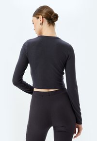 Langærmet, cropped top i mørkegrå ribbet stof. Har en rund halsudskæring og tekstureret finish, parret med matchende ribbede bukser.