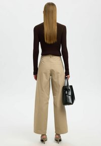 Bež hla�če širokih nogavic v kombinaciji z dolgim črnim topom z žameta. Črn nahrbtnik z vozlom dodaja piko na i videzu.