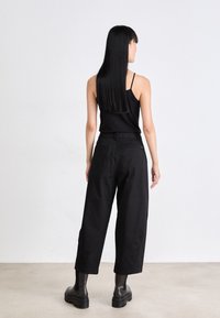 Svart tanktop, løse svarte bukser og kraftige svarte støvler. Glatt stoff, rett ben-design og minimalistiske detaljer.