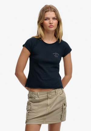 Marineblå T-shirt med korte ærmer, opbukket kant og rund halsudskæring; har et trykt logo. Kombineret med en beige mininederdel i cargo-stil.