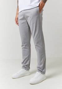 Grå bomullsbukser med slim fit, med sidelommer og mansjetter, kombinert med hvite joggesko på en nøytral bakgrunn.