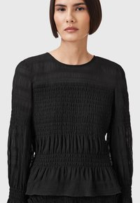 Schwarzes Peplum-Top aus strukturiertem Stoff, mit vertikalen Rüschendetails, langen Ärmeln und einem runden Halsausschnitt.