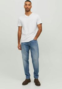 Witte v-hals t-shirt, lichtblauwe spijkerbroek, bruine enkellaarsjes. Eenvoudig ontwerp, korte mouwen, relaxte pasvorm. Denimtextuur zichtbaar in de spijkerbroek.