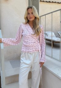 Vaaleanpunainen kimono-tyylinen paita, jossa on kukkakuosi, teksturoitu kangas, pitkät flare-hihat, yhdistettynä valkoisiin, löysiin housuihin.
