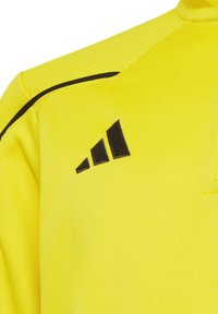 Maglietta sportiva gialla in tessuto testurizzato, con un logo nero a tre strisce sulla spalla sinistra e dettagli neri sottili.
