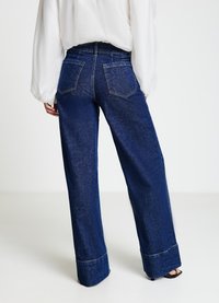 Jean denim bleu foncé à jambes larges avec une taille haute, doté de poches arrière et d'un ourlet retroussé. La texture semble lisse avec une décoloration minimale.
