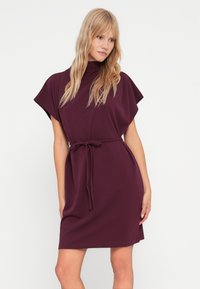 Μπορντό φόρεμα με ψηλό λαιμό και κοντές κάπες μανίκια, διαθέτει ζώνη δέσιμο στη μέση και έχει άνετη εφαρμογή, φτιαγμένο από μαλακό ύφασμα.