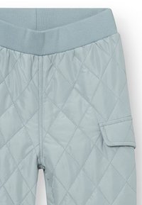 Die gesteppte hellblaue Hose verfügt über einen breiten elastischen Bund und eine seitliche aufgesetzte Tasche. Der Stoff hat eine glatte, glänzende Textur mit Rautenmuster.