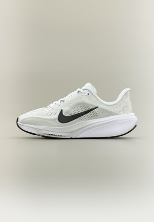 Zapatilla de running Nike Air Zoom blanca con logo swoosh negro, parte superior de malla transpirable y suela acolchada sobre fondo beige liso.
